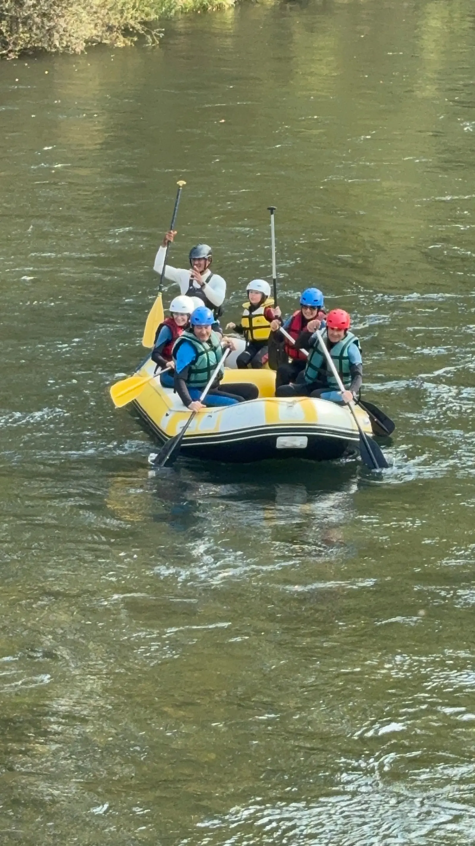 Adultos y niños con cascos y chalecos en una balsa de rafting en el río Esla.