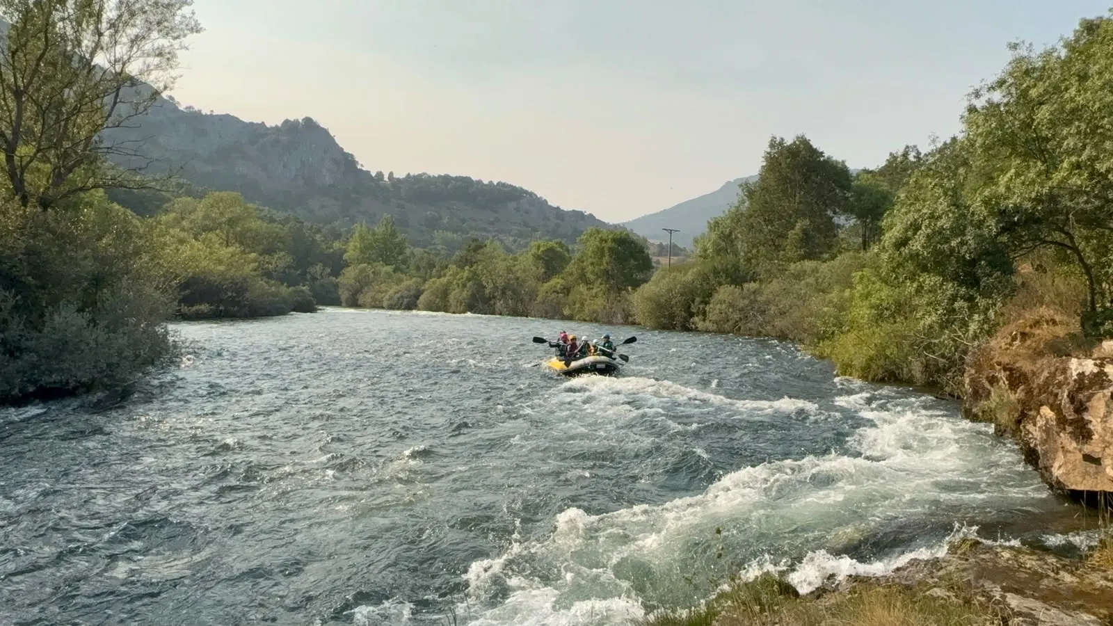 Una balsa de rafting en el Esla, con rápidos en primer plano y montañas al fondo.